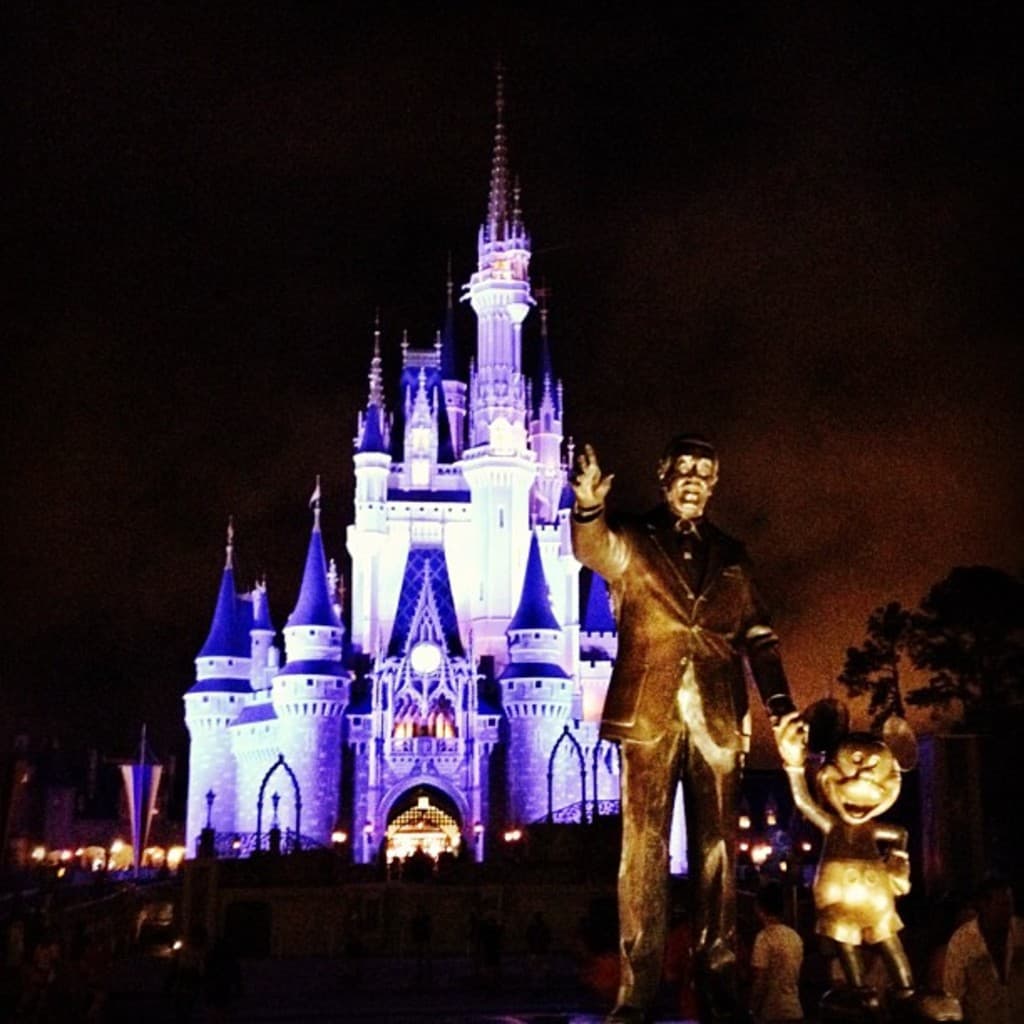 Statuen auf der rechten Seite des Bildes, mit einem Cinderella-Schloss und Bäumen im Hintergrund.