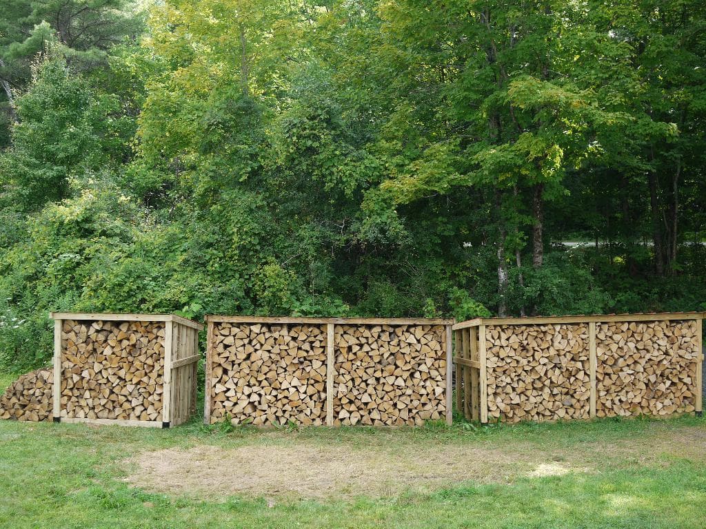Holzklötze werden in einer Kiste auf Grasboden mit Bäumen im Hintergrund gestapelt.