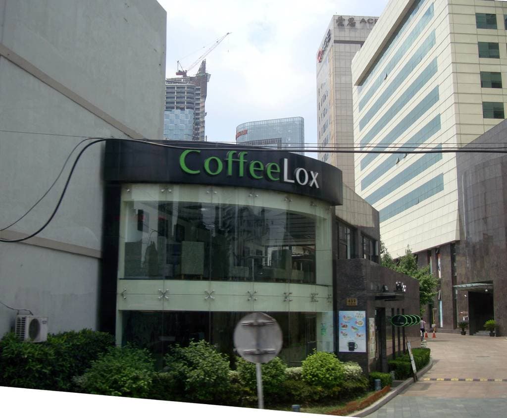 Ein Geschäftsgebäude mit einigen Pflanzen davor, umgeben von vielen hohen Gebäuden und einigen Drähten.