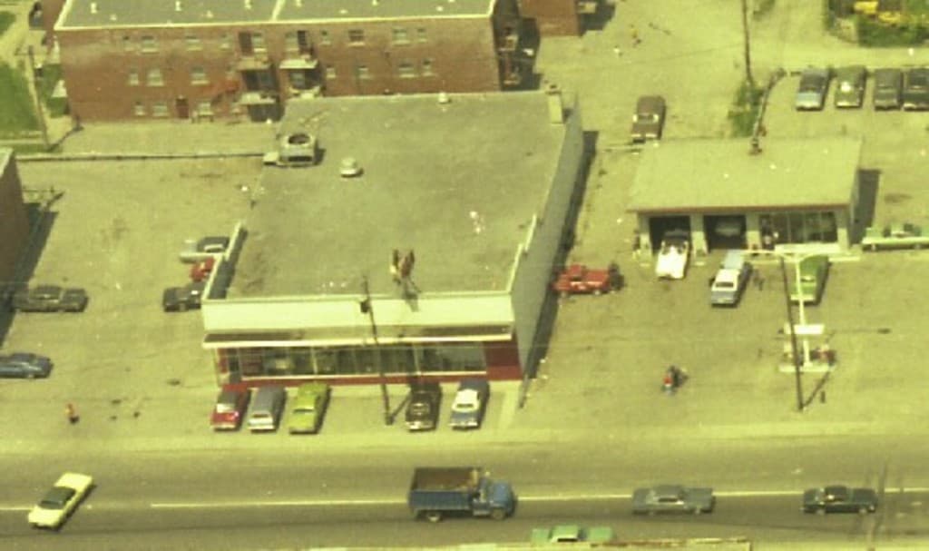 Eine Luftansicht einer Stadt mit zahlreichen Autos, die um Gebäude herum geparkt sind und einige Autos auf den Straßen fahren.