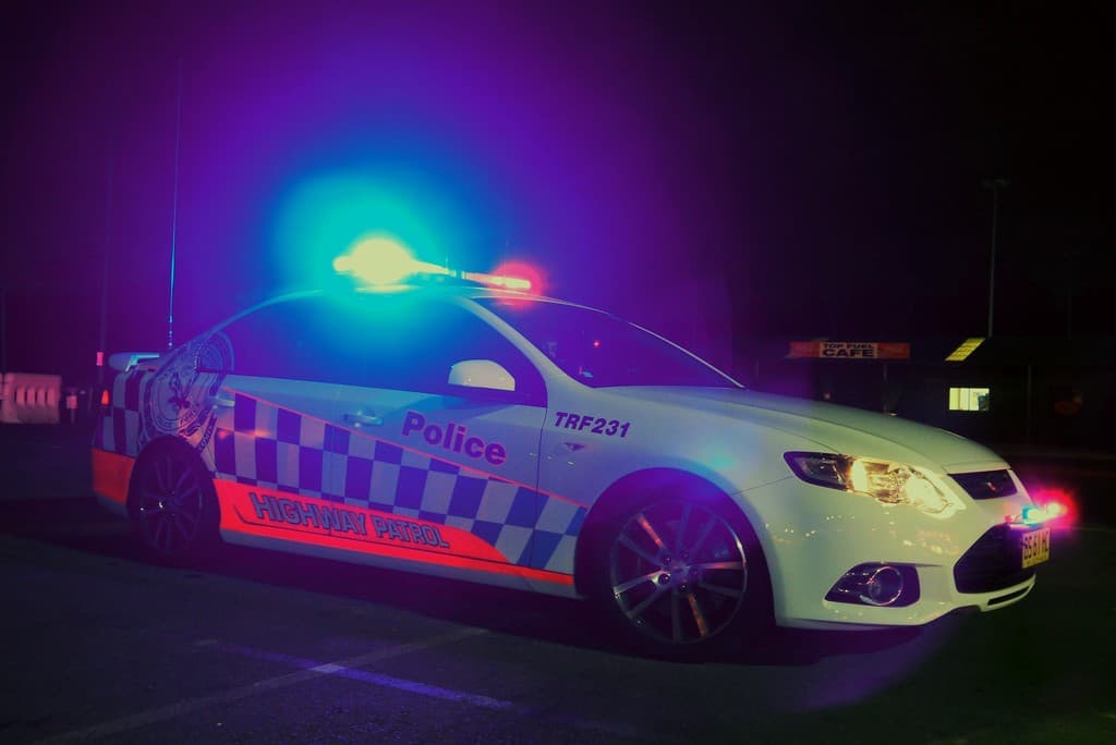 Ein weißer Polizeiwagen mit Lichtern und Aufklebern vor schwarzem Hintergrund.