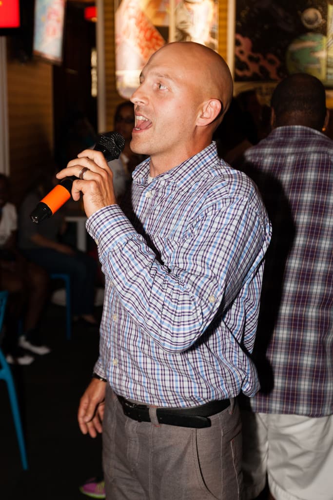 Eine Person in einem schwarzen Gürtel steht vor einem Mikrofon und singt, während eine Gruppe von Menschen hinter ihr steht.