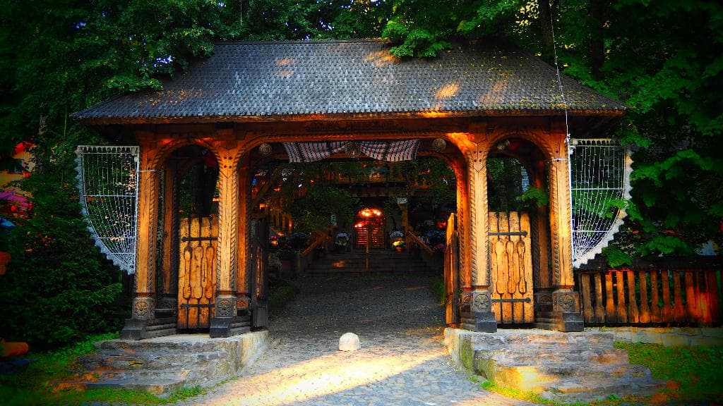 Bäume an den Ecken links und rechts, Kissen mit Dach und Tor im Vordergrund, Gebäude im Hintergrund und Straße unten.