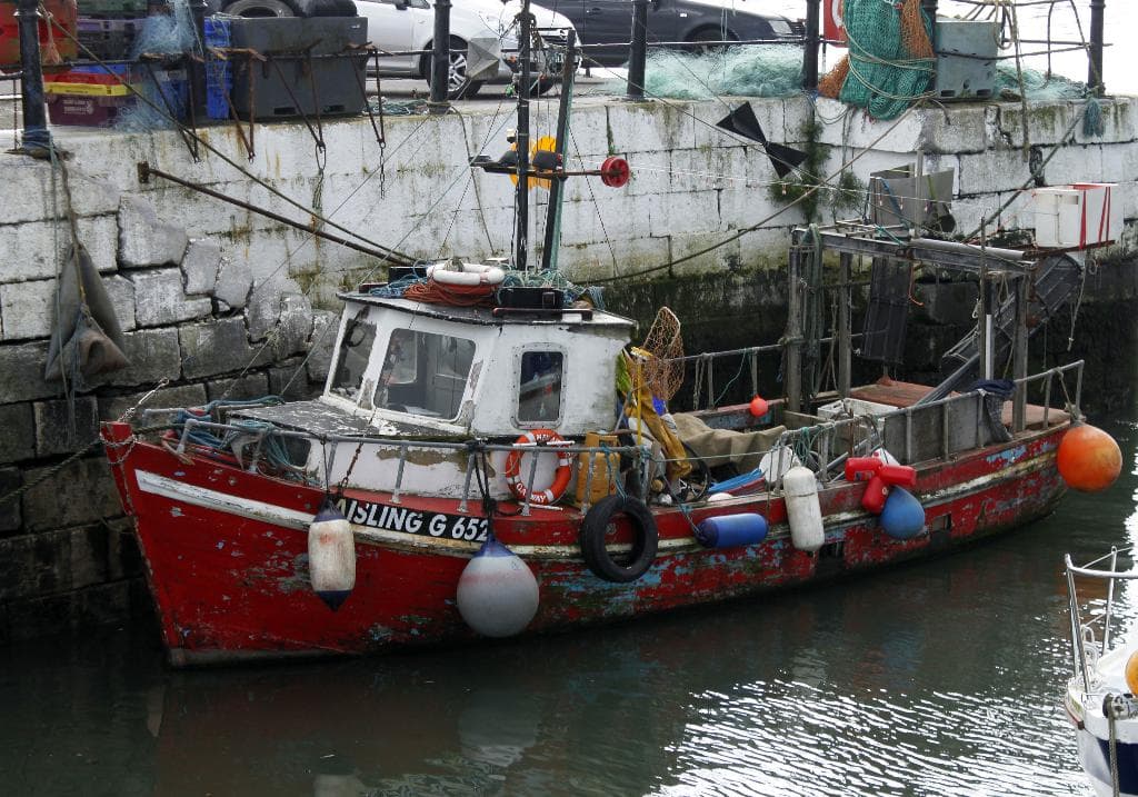 Zwei Boote auf einem Fluss, eines in der Nähe einer Wand mit einem Zaun und Pfählen, verschiedene Gegenstände auf dem Boden, zwei Autos und Gegenstände, die an den Booten und der Wand befestigt sind.