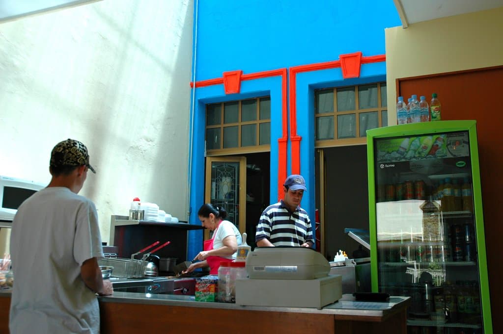 Drei Personen arbeiten in einer Küche, wobei auf der rechten Seite des Bildes ein Kühlschrank zu sehen ist.