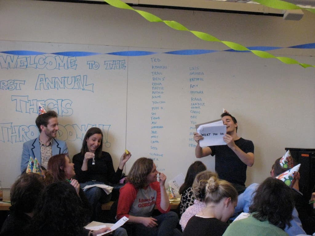 Eine Gruppe von Menschen feiert ihren ersten jährlichen Thesistag, mit Bändern geschmückt und einige tragen Mützen.