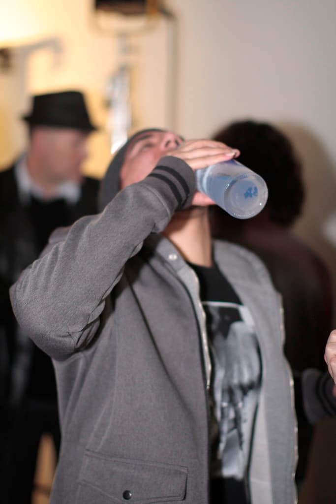 Ein Mann in der Mitte des Bildes hält eine Flasche und trinkt Wasser, umgeben von ein paar anderen Menschen.