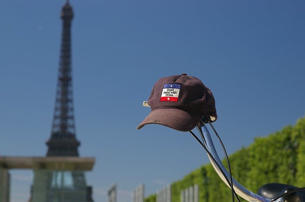 Ein Fahrrad mit einer Kappe auf dem Lenker, ein Turm links und Pflanzen rechts.