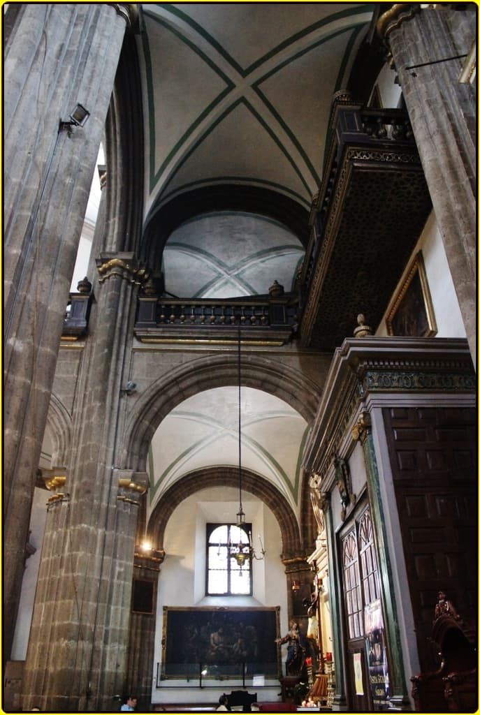 Ein Innenblick in einen Palast mit Schränken, beleuchteten Säulen, Wandskulpturen, einem großen Foto Rahmen und einer von der Decke hängenden Lampe.