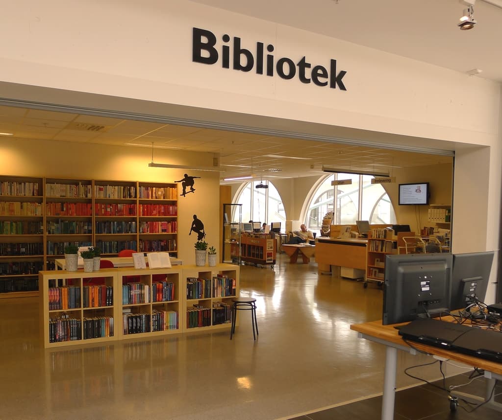 Mehrere hölzerne Regale mit Büchern, mit Monitoren auf der rechten Seite und dem Wort 'BIBLIOTECA' oben angezeigt.