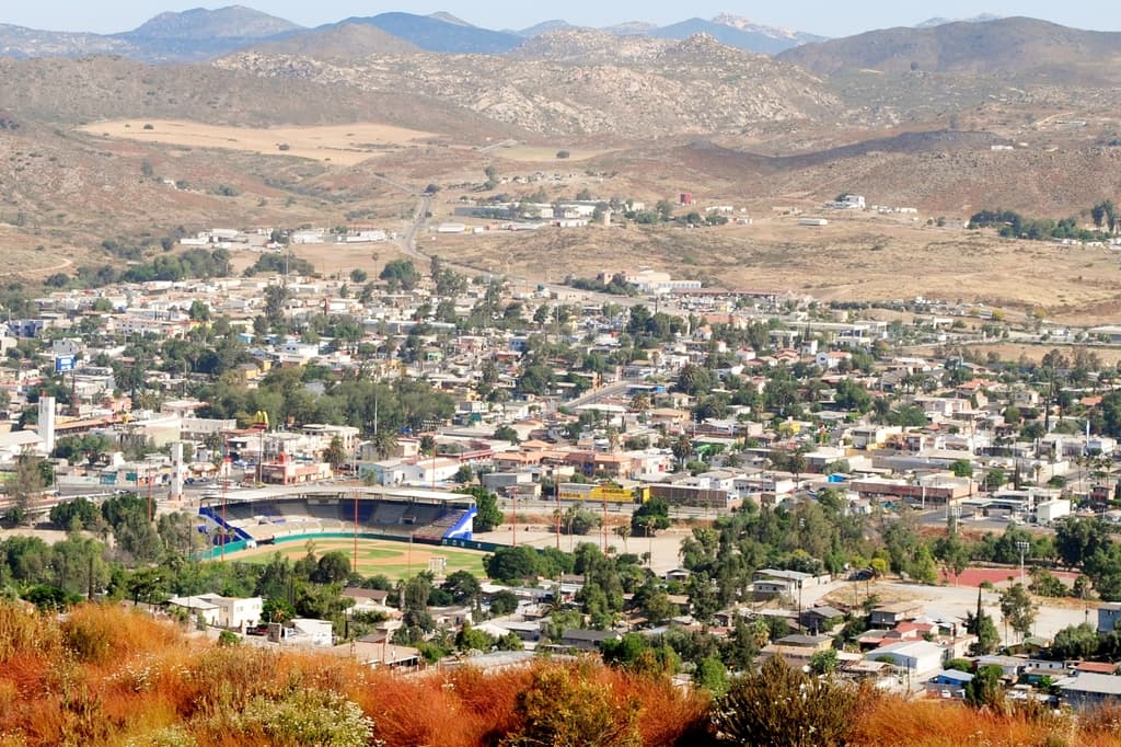 Eine Landschaft mit Häusern, Bäumen, Stromleitungen, Hügeln und einem klaren Himmel.