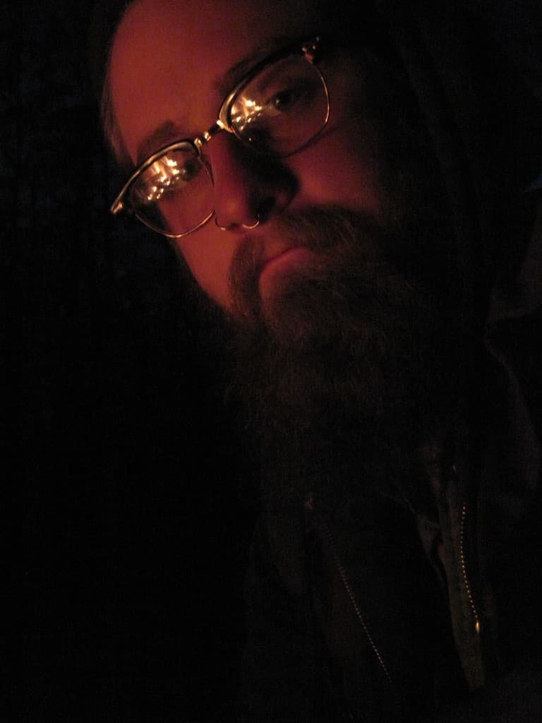 Ein Mann mit einem großen Bart und Brille posiert vor der Kamera.