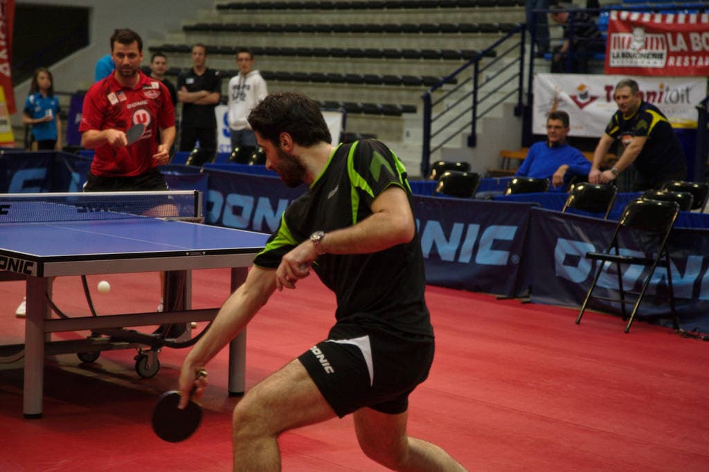 Eine Gruppe von Menschen in verschiedenen Farben, darunter schwarz, weiß und blau, versammelt sich um einen Tisch mit einem Spiel, Stühlen und einer Treppe im Hintergrund.