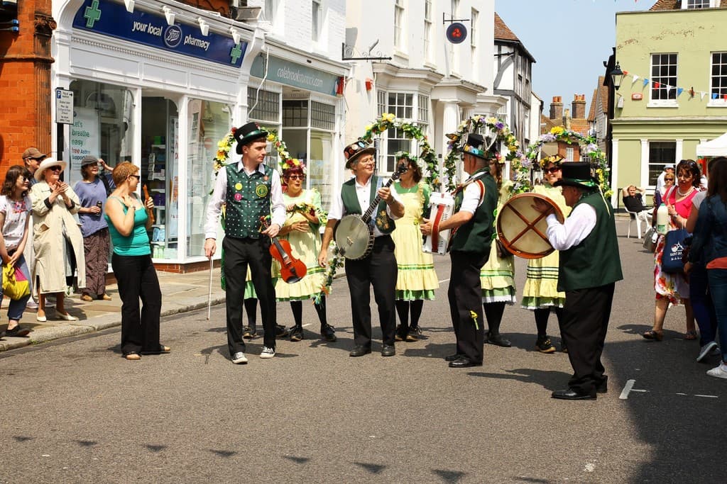Eine Gruppe von Musikern spielt Instrumente auf der Straße, umgeben von einer kleinen Menge und Geschäften mit Schildern im Hintergrund.
