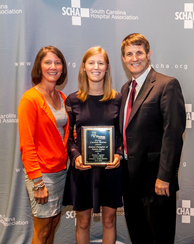 Eine Gruppe von Menschen in Sportkleidung, einige halten eine Trophäe und Blumen, posieren vor einer Menge mit Geländern und Schildern im Hintergrund.