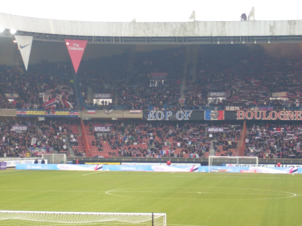 Ein Rasenplatz mit Torpfosten auf beiden Seiten, Zuschauern im Hintergrund und zahlreichen Werbetafeln in der Mitte und oben.