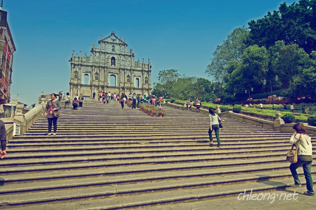 Ein Denkmal mit vielen Stufen davor, umgeben von zahlreichen Menschen und Bäumen auf der rechten Seite.