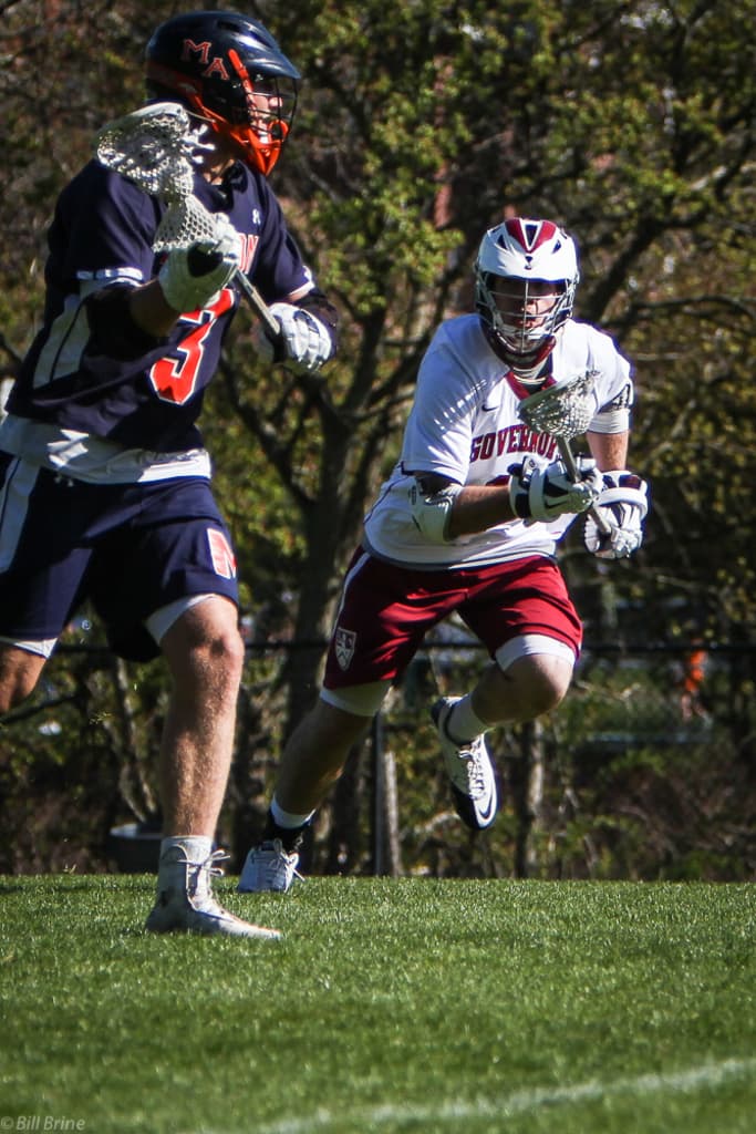 Zwei Spieler mit Helmen und Schlägern auf einem Feld mit Bäumen im Hintergrund.