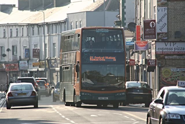 Eine Straße mit Autos und einem Bus vor Gebäuden mit Wänden, Fenstern, Tellern und Dächern, mit Plakaten und Bannern an den Wänden und einem Pfosten mit einer Straßenlaterne.