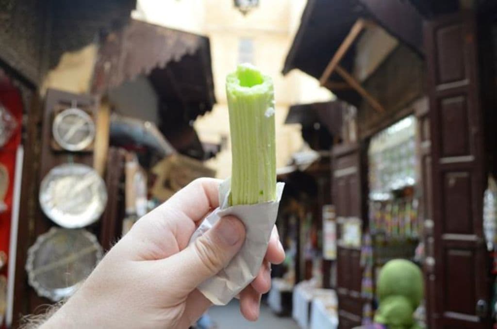 Eine Hand im Bild hält ein Objekt, im Hintergrund sind Häuser und Geschäfte zu sehen.