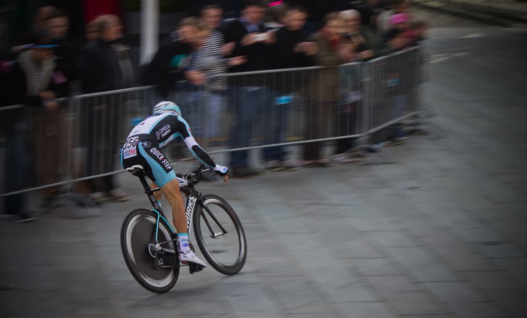 Eine Person fährt ein Fahrrad bei einem Rennen mit Zuschauern hinter einem Zaun links