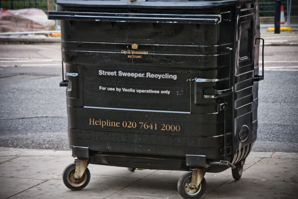 Ein schwarzer Mülltonnen ist in der Mitte des Bildes mit einer Straße unten.