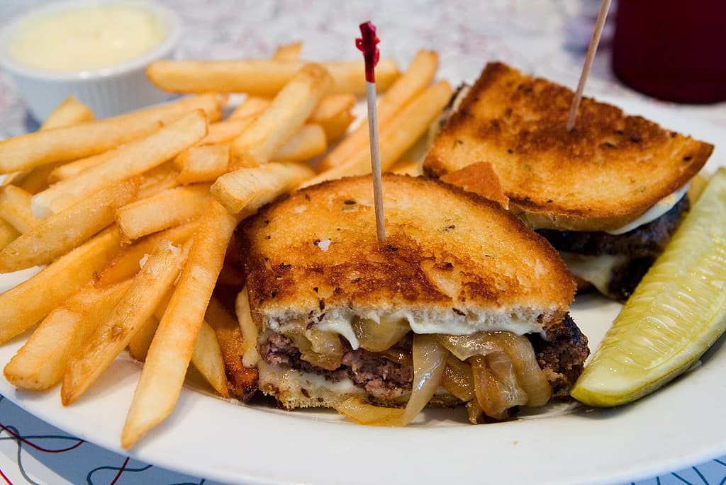 Ein weißer Teller mit Pommes frites, Burgern und einer Schüssel in der oberen linken Ecke.