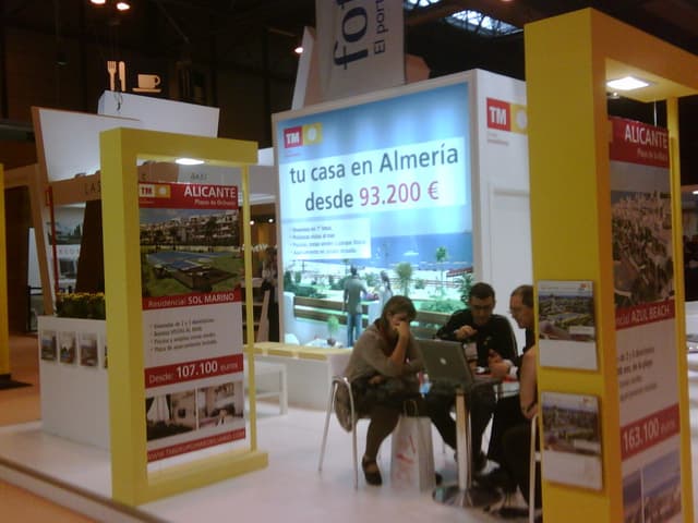 Ein Raum mit Menschen, die an einem Tisch arbeiten, umgeben von mehreren Flyern mit verschiedenen Anzeigen.