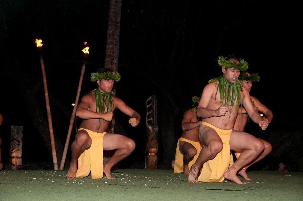 Vier Männer tanzen auf einer Bühne mit einem Stock und einer Wand im Hintergrund.