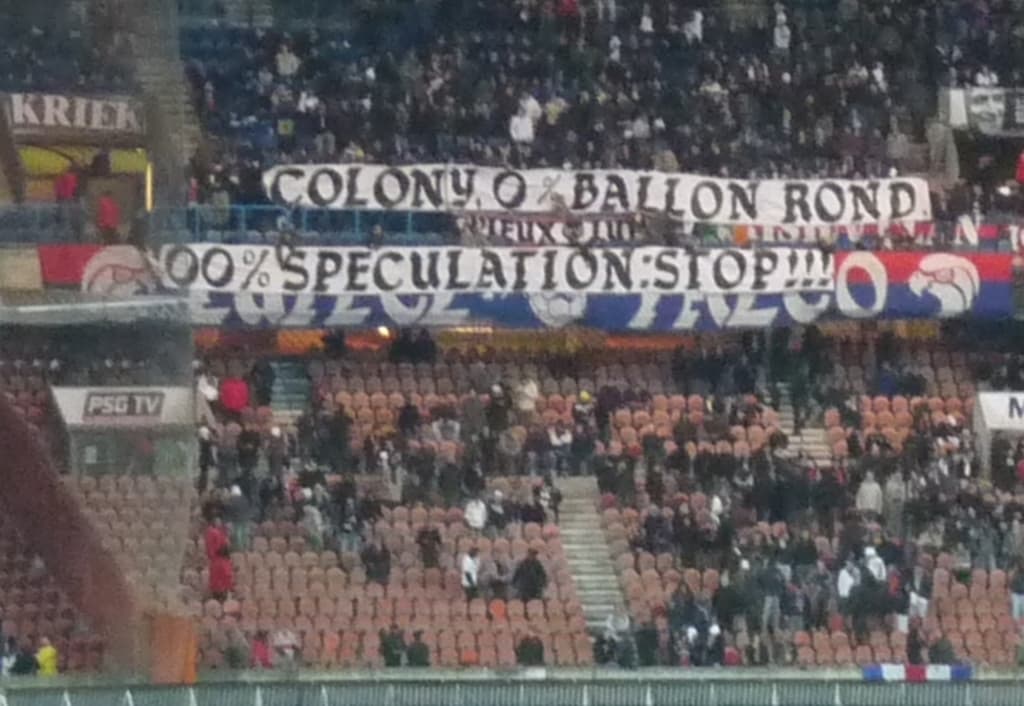 Ein Stadion voller großer Menschenmenge, Banner und Stühle, mit einem Zaun unten und einer Treppe links.
