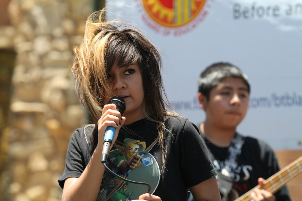 Eine Frau, die auf der Bühne Gitarre spielt und singt, mit einer Band im Hintergrund und einem Bildschirm an der Wand dahinter.