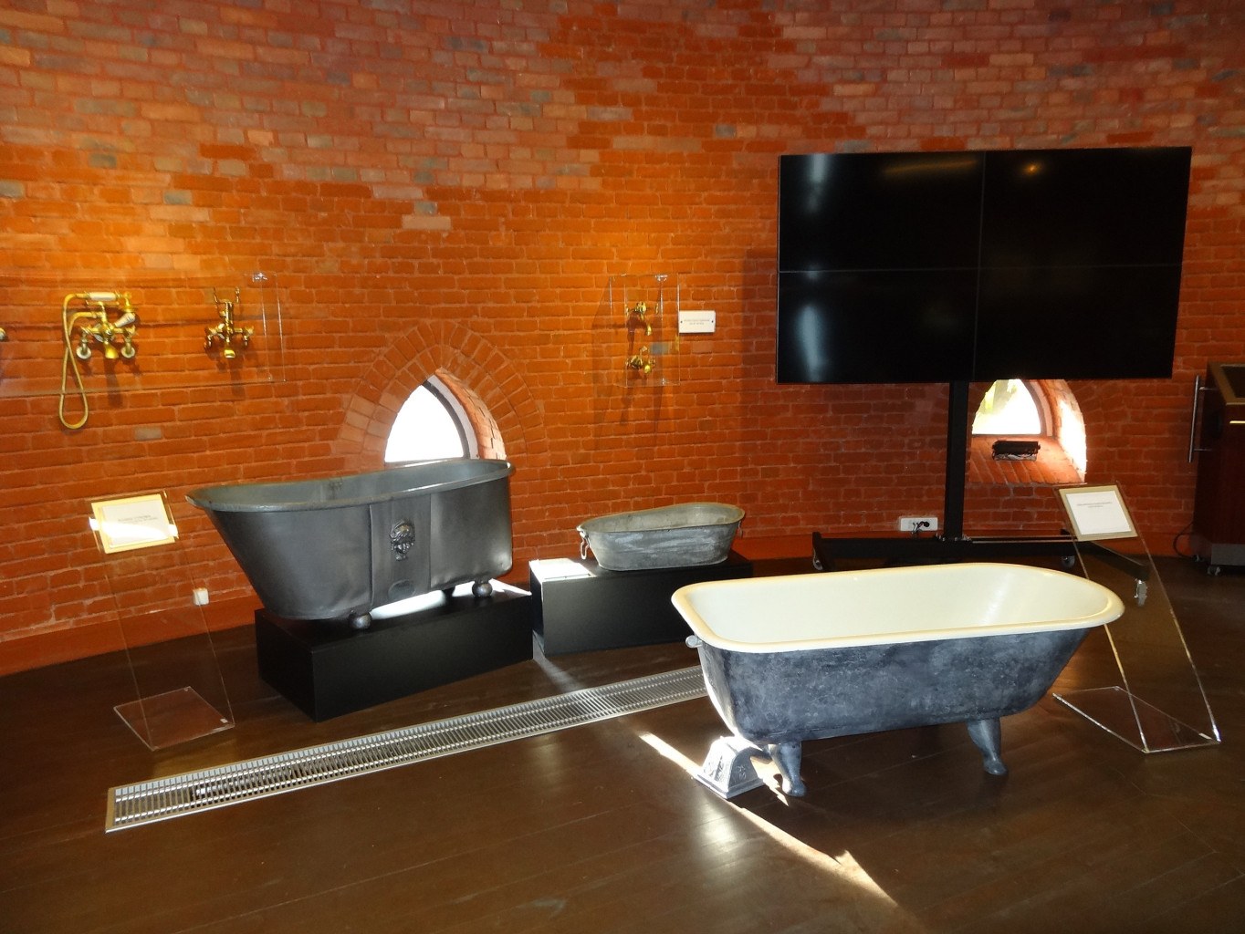 Ein gemütliches Badezimmer mit einer Backsteinwand, einer zentralen Badewanne, an der Wand montierten Armaturen auf der linken Seite und einem an der Wand montierten Fernseher auf der rechten Seite.