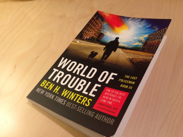 Ein Buch mit dem Titel 'World Of Trouble' mit einem Mann und einem Hund auf dem Cover, das auf einem Tisch liegt.