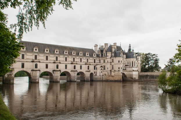 Ein Schloss auf dem Wasser mit Bäumen im Hintergrund, Wasser unten und Himmel oben.