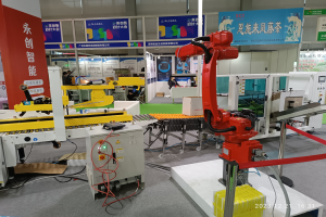 Eine Gruppe von Robotern auf einem Tisch umgeben von Maschinen und elektronischen Bauteilen, mit ein paar Menschen im Hintergrund in einer Fabrikumgebung.