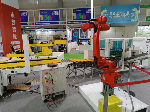 Eine Gruppe von Robotern auf einem Tisch umgeben von Maschinen und elektronischen Bauteilen, mit ein paar Menschen im Hintergrund in einer Fabrikumgebung.