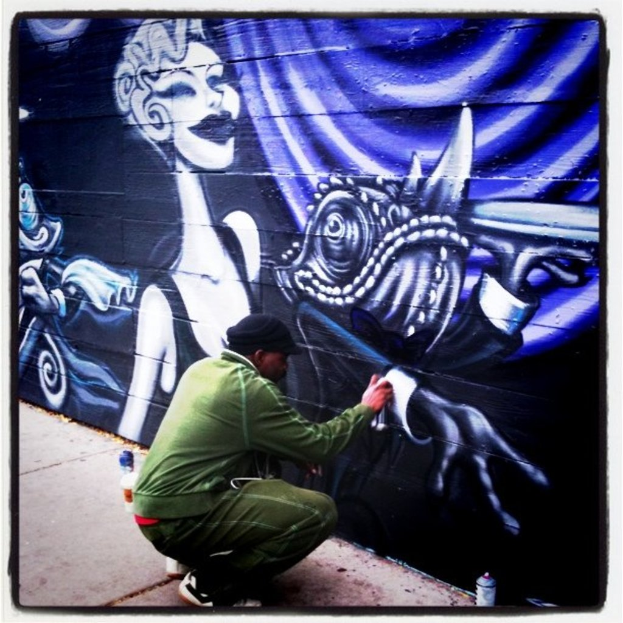 Eine Person mit einer Flasche auf einer Straße mit anderen Flaschen drumherum, mit einer mit Graffiti bedeckten Wand im Hintergrund.