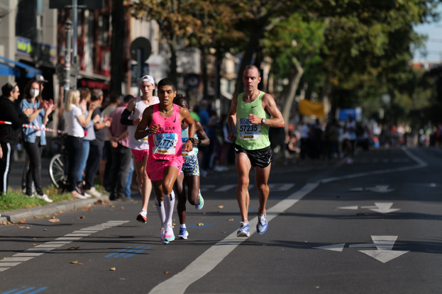 Gruppe von Menschen, die in einem Stadtmarathon auf einer Straße laufen, mit Zuschauern und unscharfem städtischem Hintergrund.