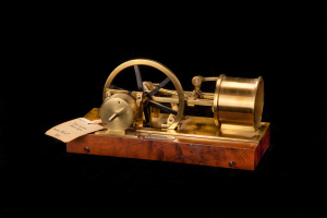 Altmodische Uhr mit Holzunterteil, Metallrad und Papieraufsatz vor schwarzem Hintergrund, möglicherweise als Zeitumschalter fungierend.