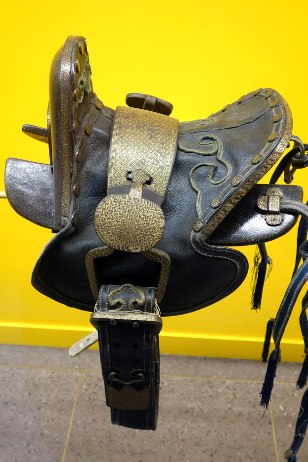 Nahaufnahme eines Pferdesattels auf einem Regal in einem Geschäft vor einer gelben Wand.