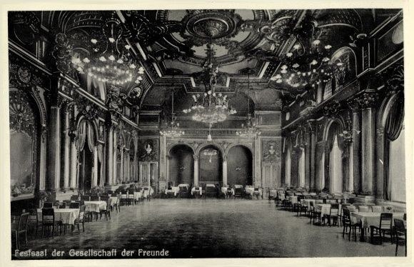 Ein altes Schwarz-Weiß-Foto eines großen Raums mit Tischen, Stühlen, Säulen, Bögen und Kronleuchtern an der Decke, mit Text unten, der "Festival der Gesellschaft der Freunde, Berlin" lautet.