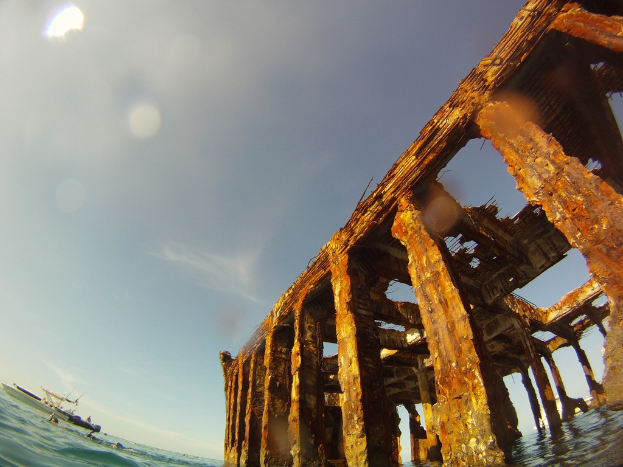 Ein Schiff befindet sich auf dem Wasser in der linken unteren Ecke, mit einem hölzernen Dock auf der rechten Seite.