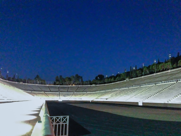Olympiastadion bei Nacht, beleuchtet von Stadionlichtern und Sternen, umgeben von Bäumen und Pfählen, mit Boden im Vordergrund.