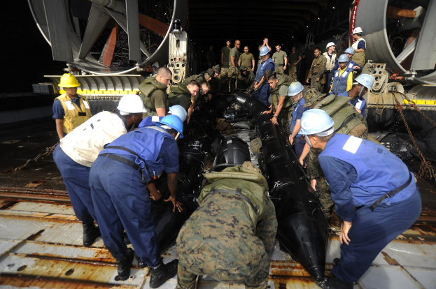 Eine Gruppe von M├Ąnnern in harten Helmen und Uniformen, die an einem U-Boot in einem Schiffbauwerk arbeiten.