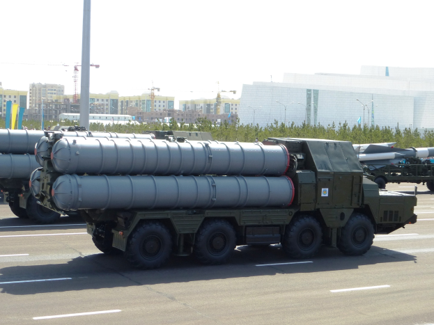 Militärlastwagen transportiert eine Rakete auf einer Straße mit Bäumen, Strommasten, Gebäuden und einem klaren blauen Himmel.