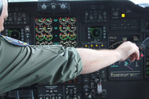 Ein Mann in einer Pilotenuniform sitzt in einem Flugsimulator-Cockpit und hält ein Objekt in der Hand, umgeben von verschiedenen Messgeräten und Ausrüstungen.