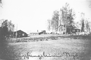 Ein Schwarz-Weiß-Foto eines Bauernhofs mit Häusern, Bäumen, Pfählen, Pflanzen und Gras im Vordergrund und einem Himmel im Hintergrund, mit dem Text "Hans Christian Meyers Bauernhof in den frühen 1900er Jahren" unten.