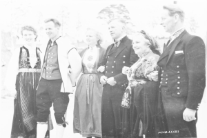Eine Gruppe von Menschen in den 1930er Jahren, die zusammenstehen, lächeln, mit Bäumen im Hintergrund und dem Text "Bayerische Familie in den 1930er Jahren" unten.
