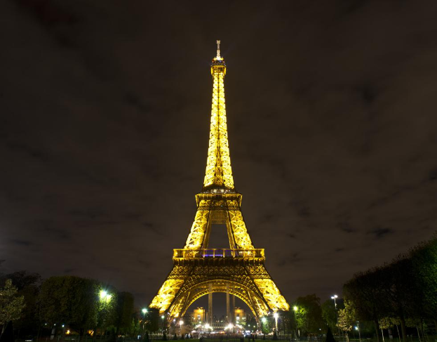 Der Eiffelturm ragt mit Bäumen und Lichtmasten an seiner Basis in den Himmel.