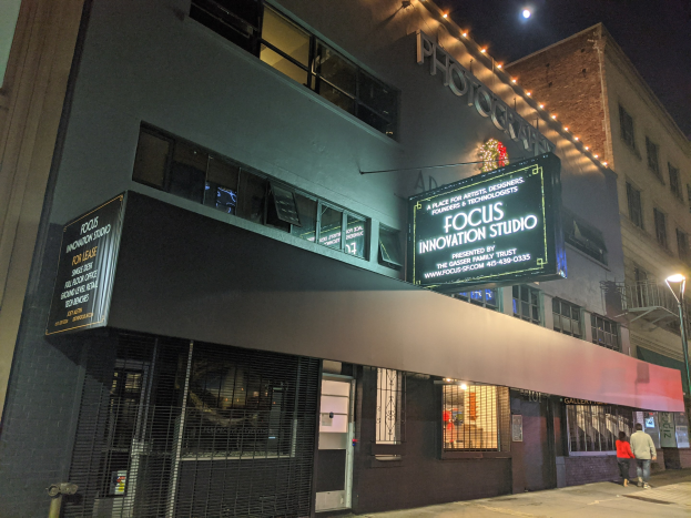 Außenansicht des Focus Innovation Studios in New York City bei Nacht, mit beleuchteten Fenstern, einer Straßenbeschilderung und Passanten auf dem Gehweg unter Straßenbeleuchtung.